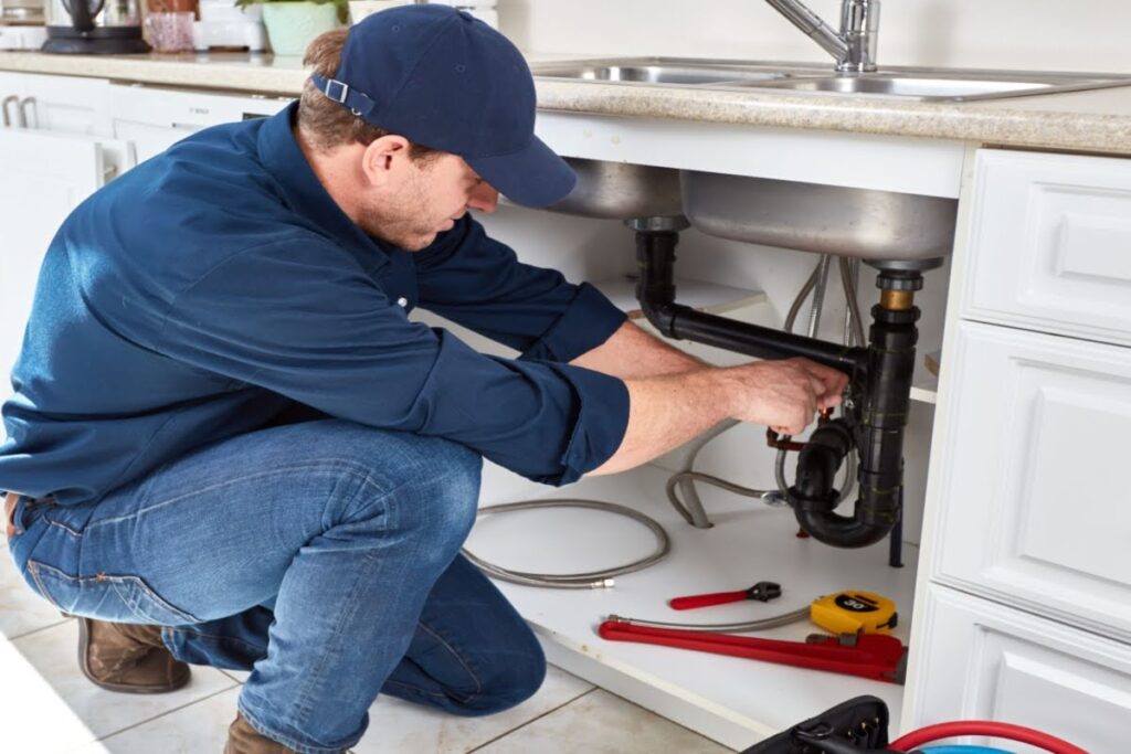 Professional plumber fixing pipes under the kitchen sink