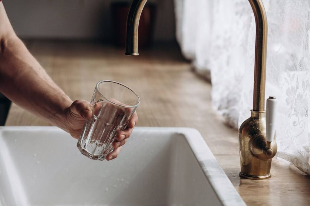 A man holding an empty glass under a kitchen faucet that has no running water