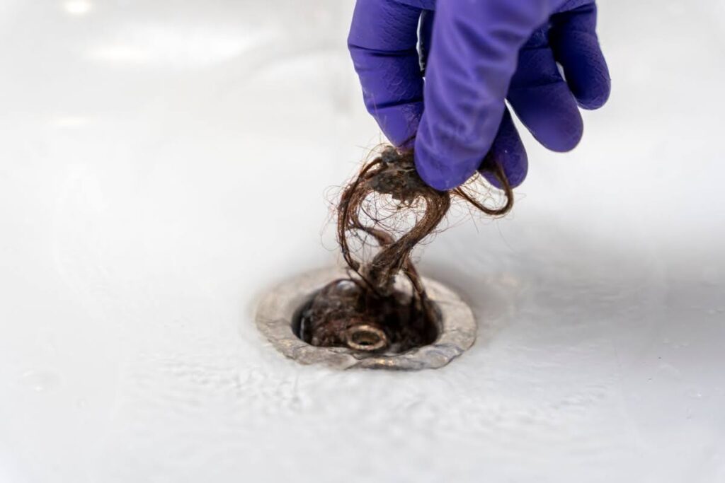 A gloved hand pulling a clump of hair out of the drain