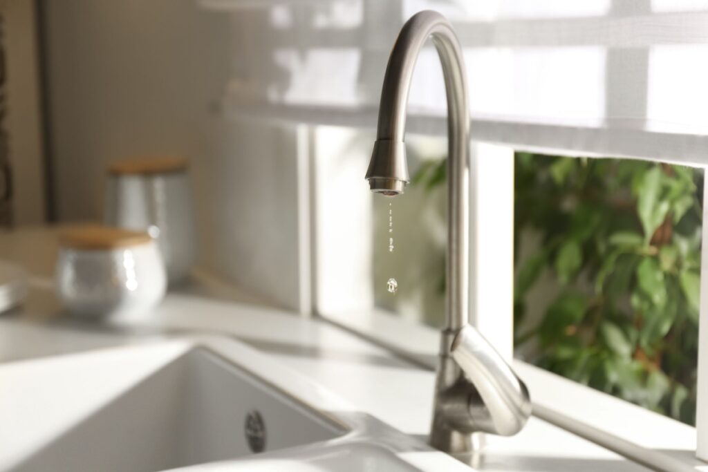 A kitchen faucet with dripping water - a sign that it has a leak